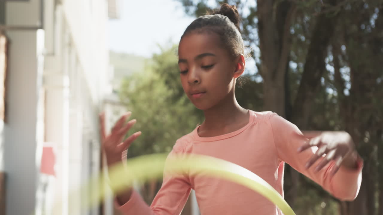 Playing with hula hoop, African American girl enjoying outdoor activity outside school