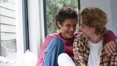 portrait of happy diverse gay male couple embracing and smiling at home, slow motion