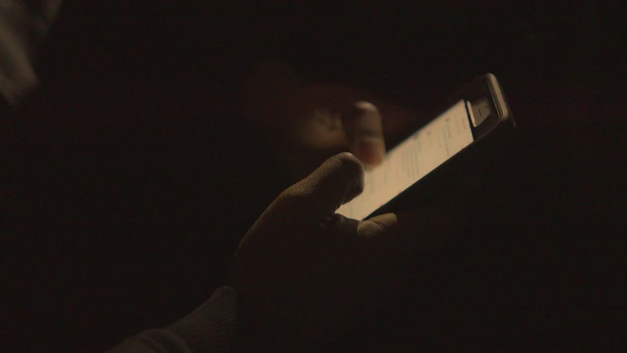vicino a una mano di un uomo nero che scorre il suo telefono al buio