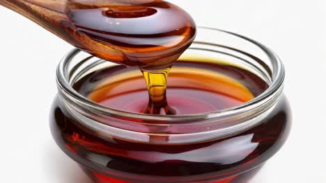 honey or maple syrup being poured from a wooden spoon into a glass jar