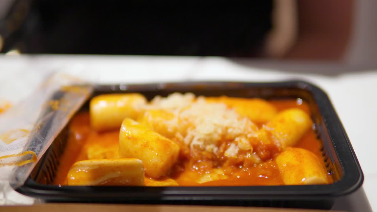 la mano de la mujer escoge el tteokbokki picante coreano - pasteles de arroz picantes en salsa picante - enfoque selectivo de primer plano