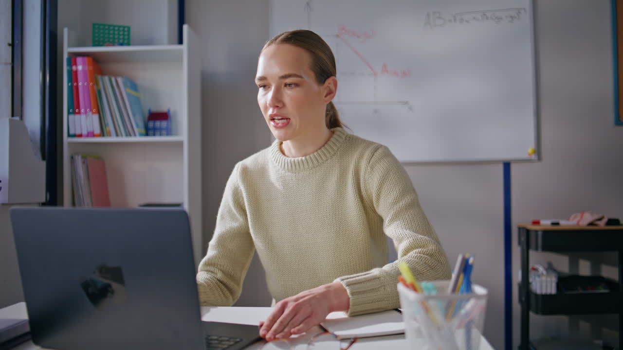 Young teacher online lesson using laptop greeting students at class room closeup