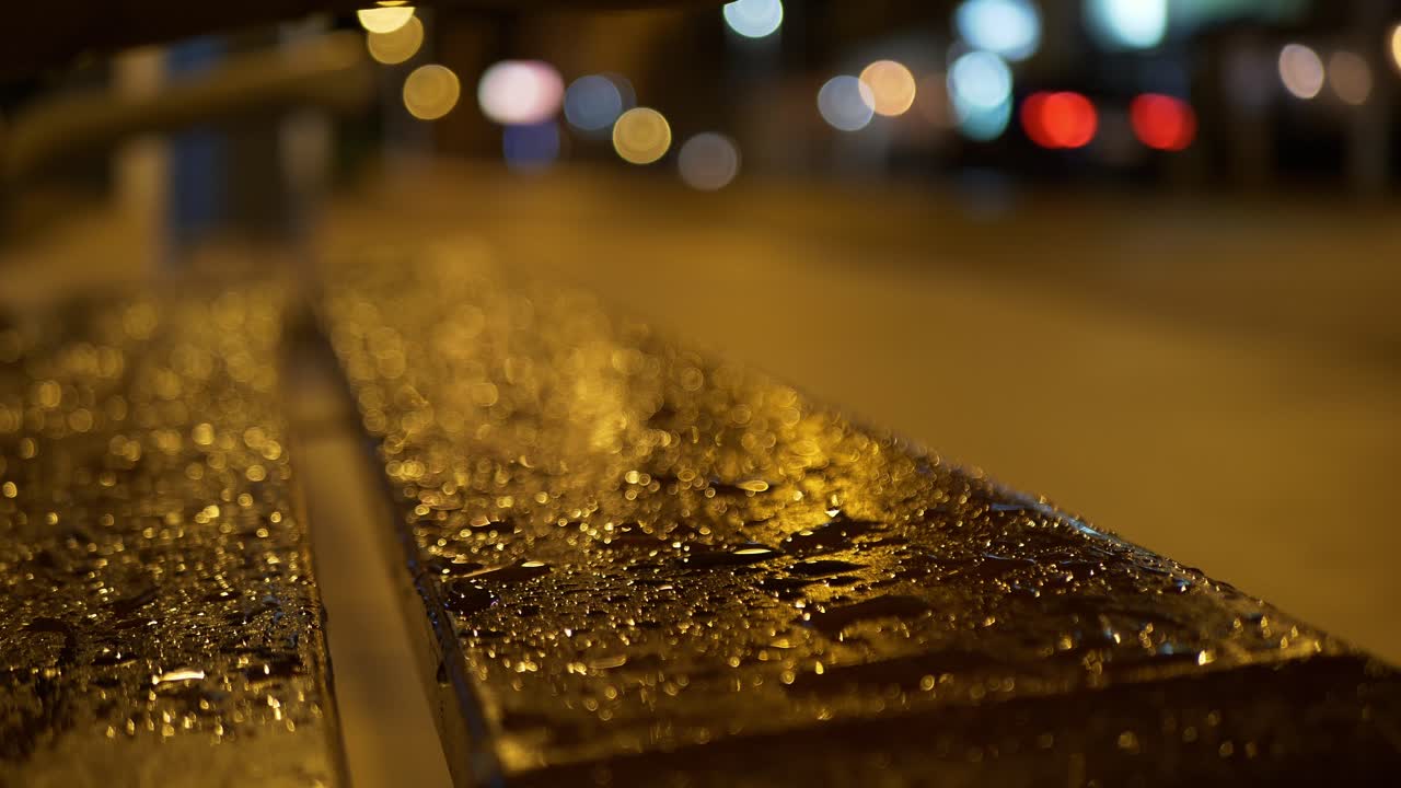 gotas de lluvia en un banco por la noche. coches pasando.