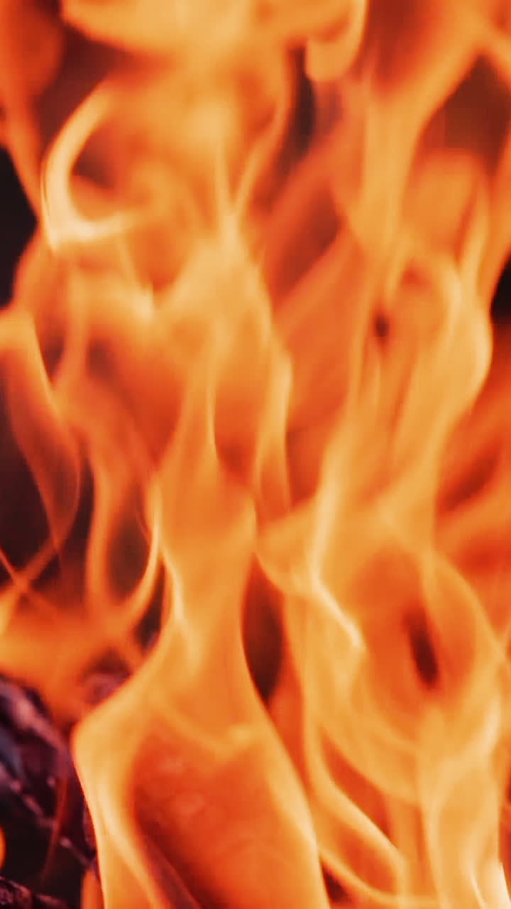 Bright flame of fire. Orange tongues of a campfire dancing on dark background. Blazing bonfire outside. Close-up. Vertical video