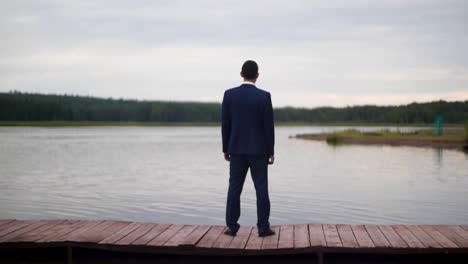 man in a suit standing on a wooden dock by a lake