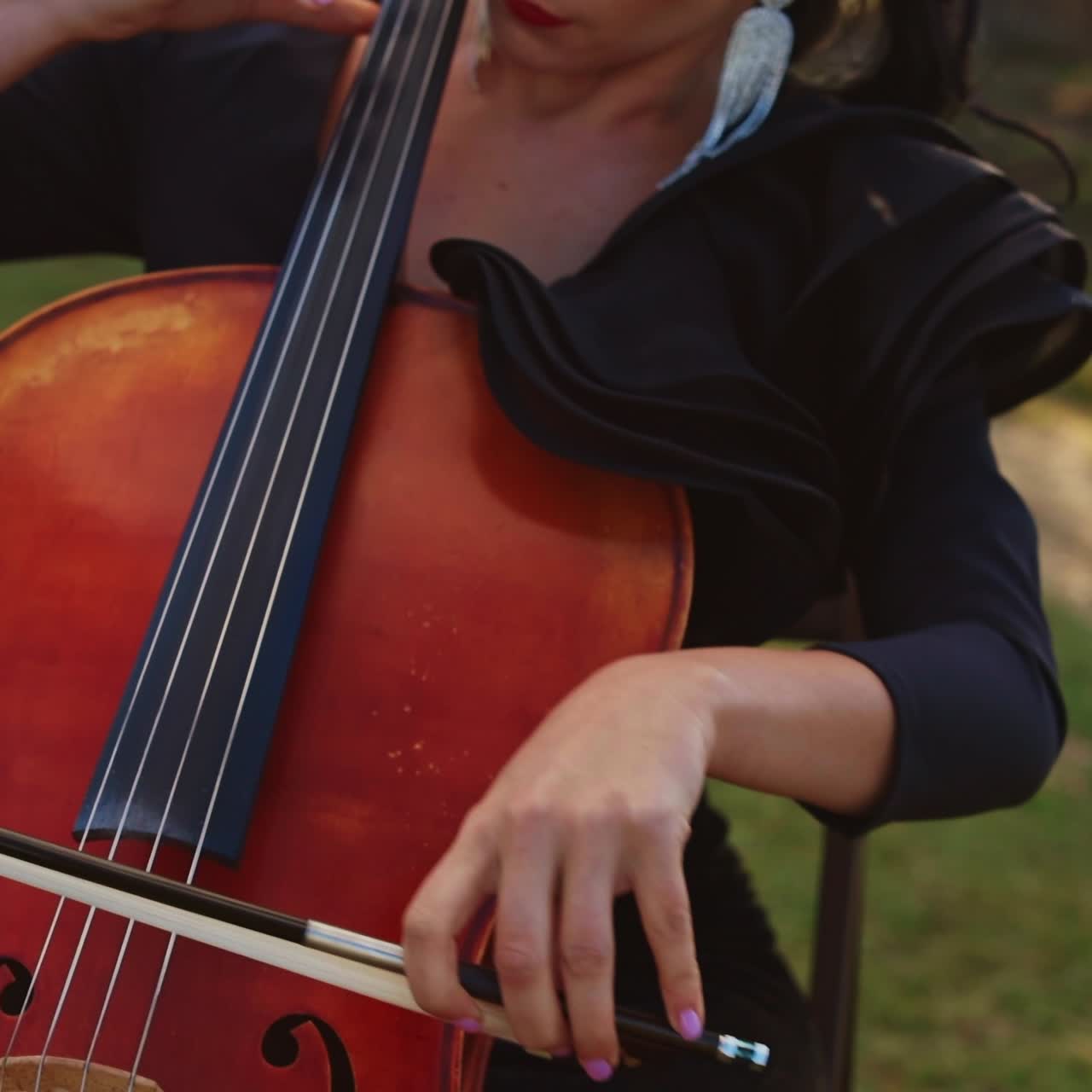 Young adult woman performing her cello play at the nature. Female music player closes her eyes enjoying music. Beautiful sunny day nature backdrop