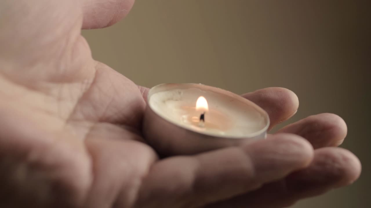 Macro di una candela da tè accesa tenuta tra le dita