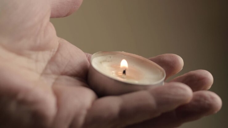 Macro di una candela da tè accesa tenuta tra le dita