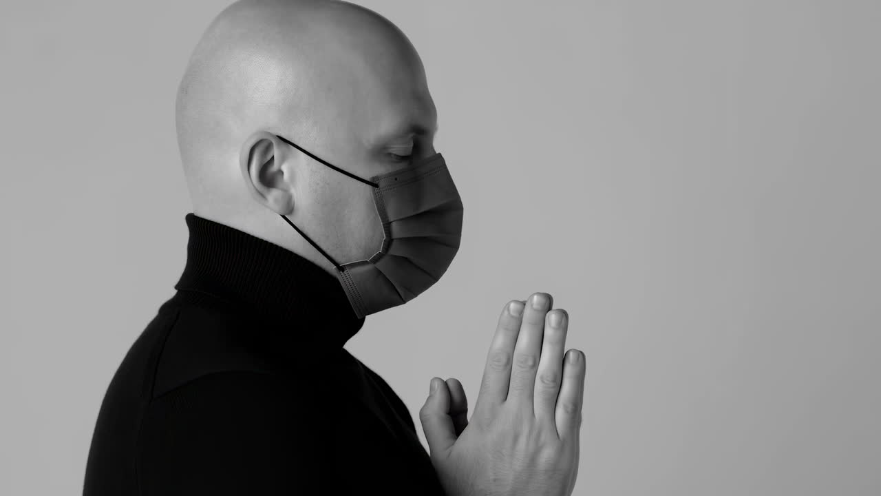 Homme chauve priant avec un masque sur le visage et les yeux fermés