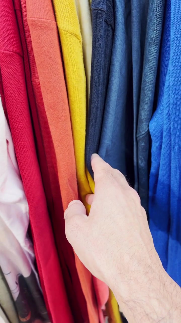 POV hand looking at clothes on a rack in vintage shop or second hand store. Person browsing fashion wear in sustainable lifestyle zero waste used clothes. Thrift store responsible shopping. Vertical