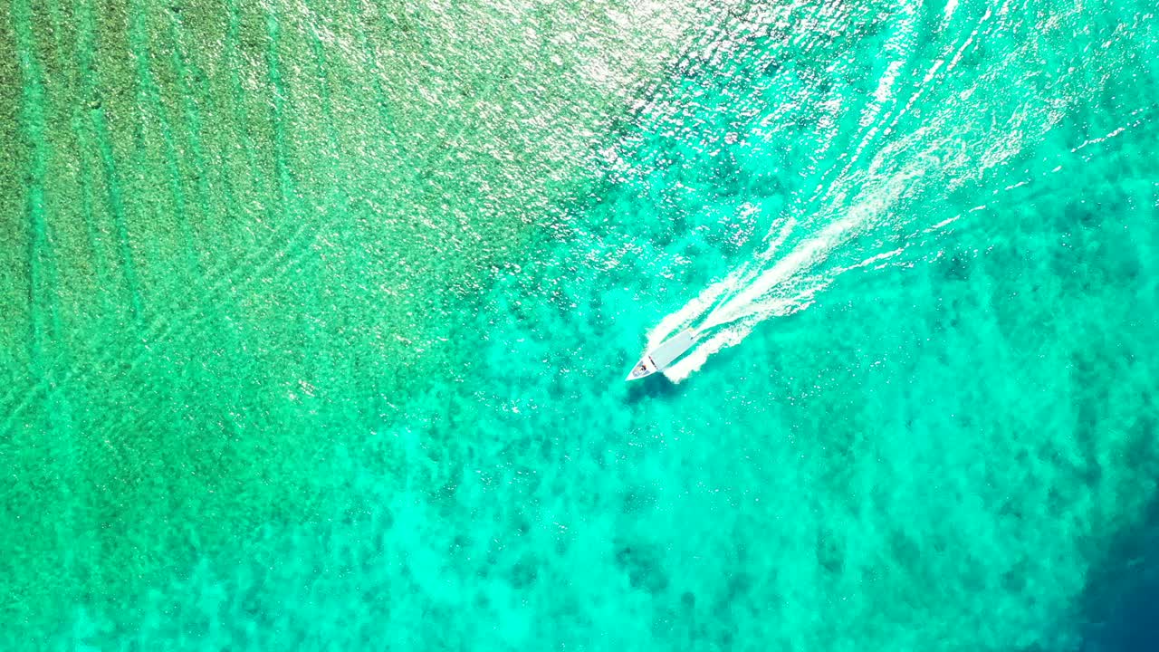 Touring boat tracing across beautiful sea surface textured with green, turquoise and blue colors of water over coral reefs and rocks seen on sea bottom in Malaysia