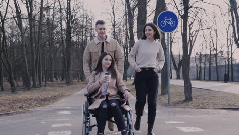 Front-View-Of-Woman-And-Man-Taking-A-Walk-With-Her-Disable-Friend-In-Wheelchair-Around-The-City