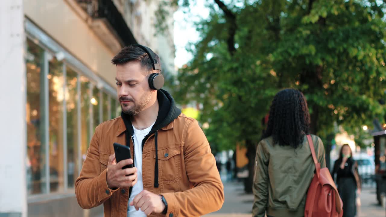 hombre barbudo caucásico con auriculares escuchando música con smartphone y bailando en la calle