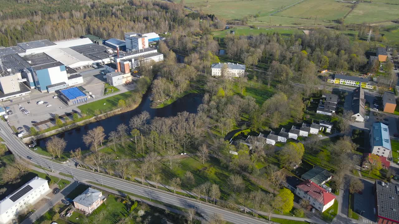 Aerial drone footage panning and flying over Saku residential urban street area during a sunny spring evening or golden hour. Small houses, apartment building and cars driving on streets visible.