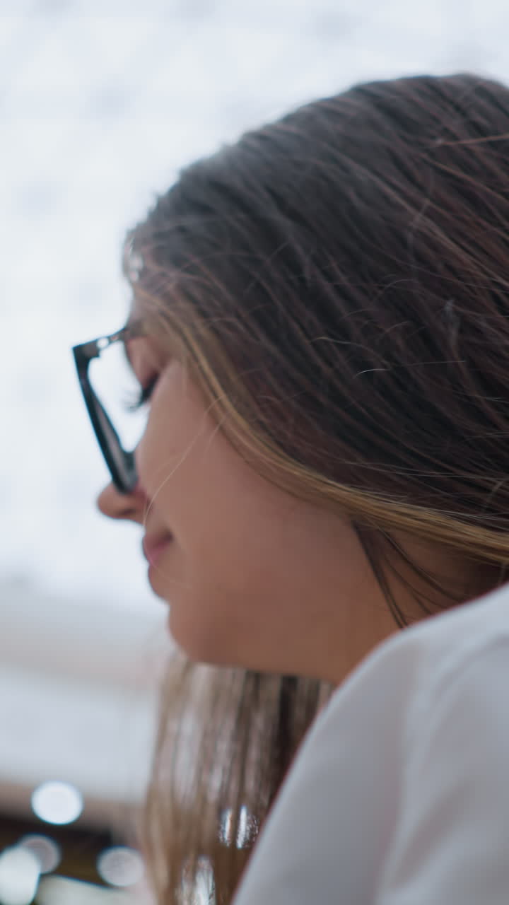 primer plano de una joven con gafas en una escalera mecánica en un centro comercial concurrido, en un estado de ánimo reflexivo mientras mira hacia la derecha, capturando su expresión contemplativa