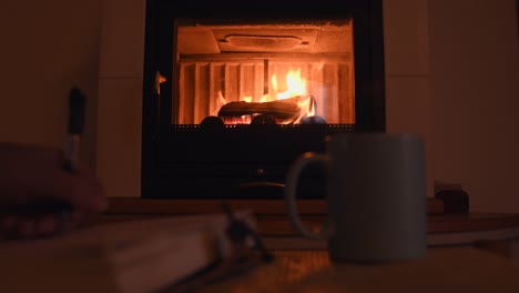 cozy background of a young female hand writing on a old notebook near a warm fireplace, with a cup with hot steam getting out of it