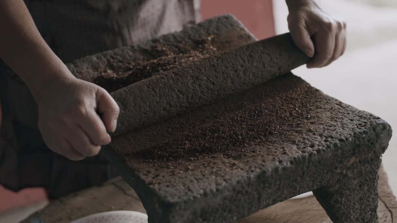 Slow motion footage of person slowly grinding coffee beans into a fine ground on a volcanic stone
