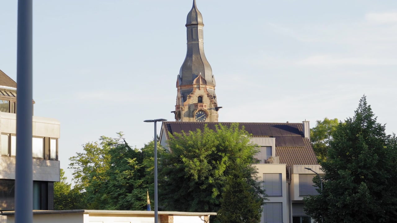 Carros estacionados em uma área urbana com edifícios e uma torre de igreja histórica ao fundo em Saarlouis, Alemanha