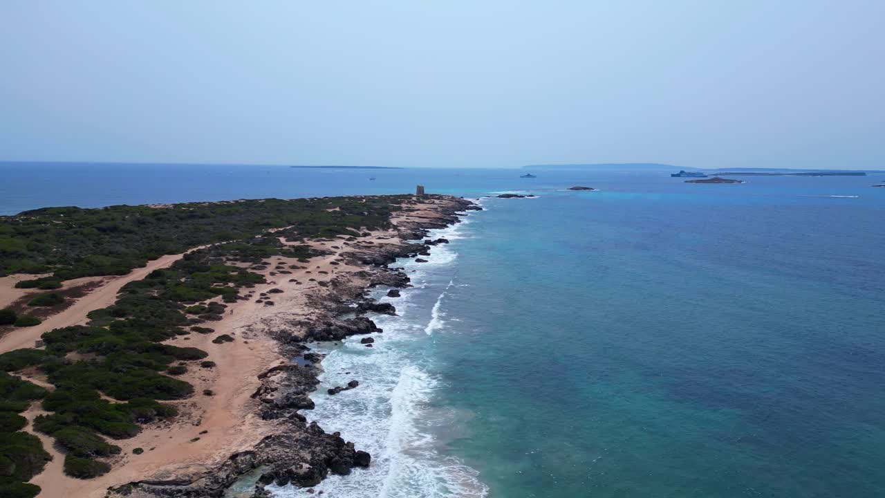 Turquoise waves crashing on the rocky coast of Ses Salines beach with the ancient watchtower. Stunning aerial view flight overflight flyover drone