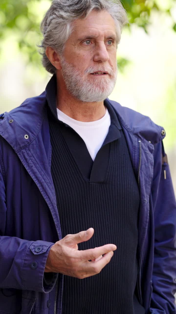 Portrait of an older man with grey hair and beard wearing a jacket and sweater