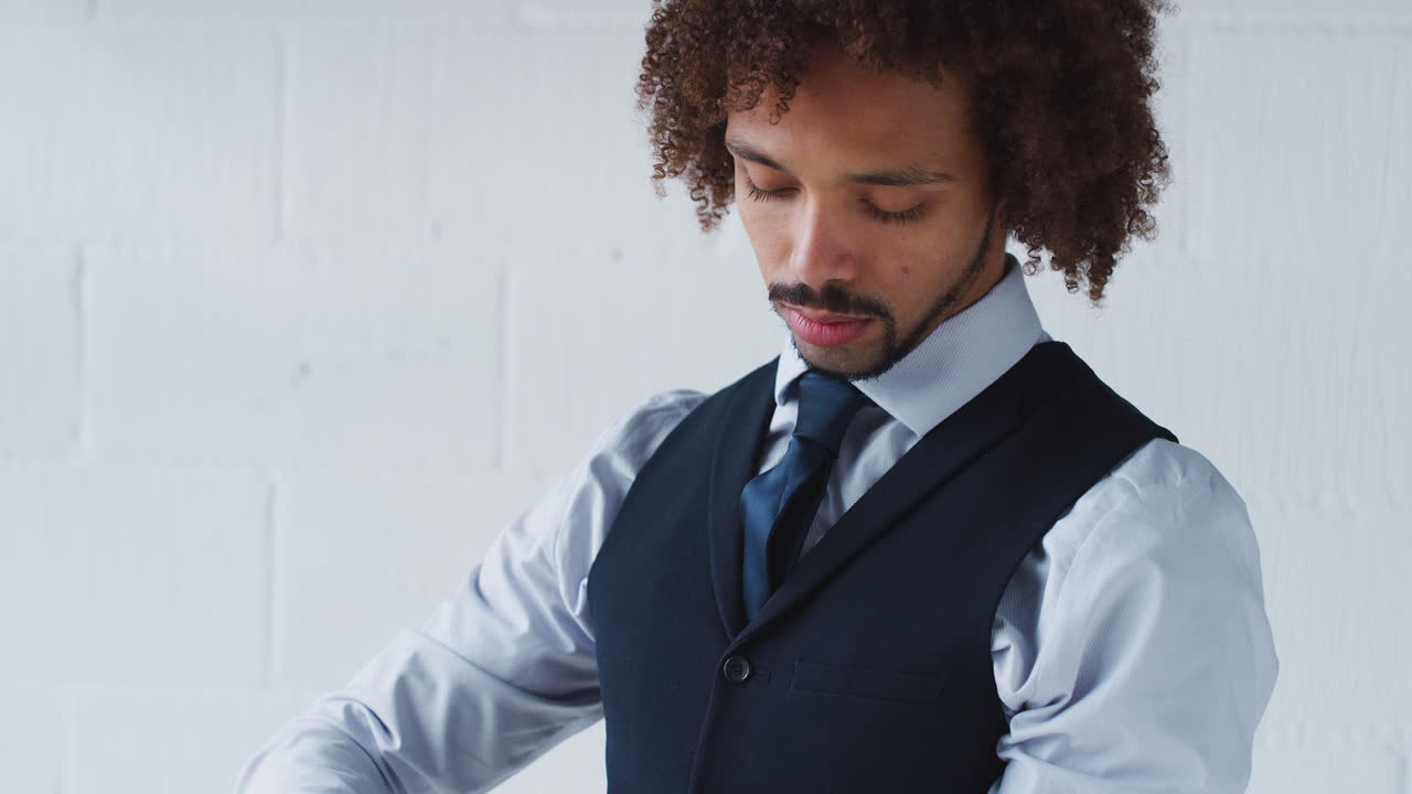 retrato de un joven empresario en traje atando un reloj de pulsera de pie contra la pared blanca del estudio