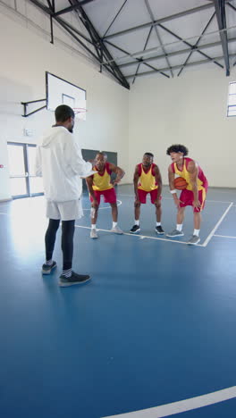 vertical video: basketball coach instructing male players on court during practice session