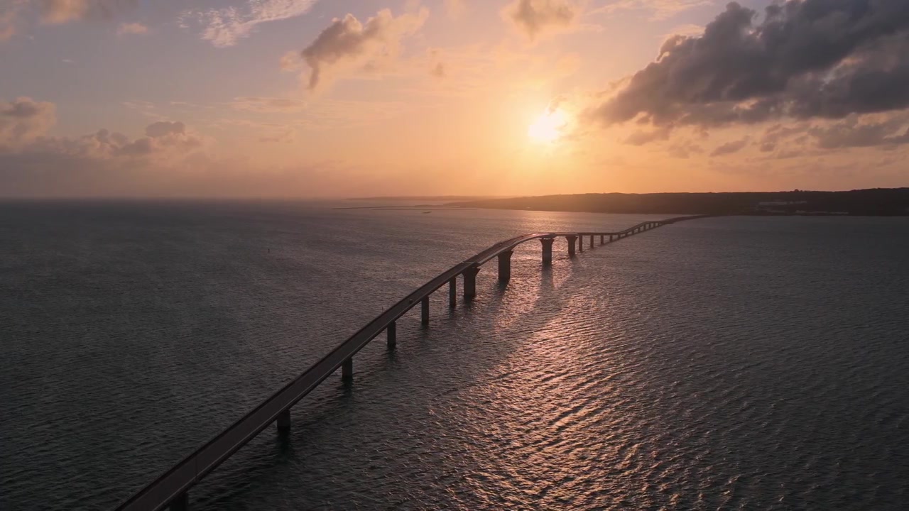 Riprese aeree orizzontali con panoramica a sinistra e movimento a destra sopra il Ponte Irabu al tramonto, con luce dorata che si riflette sull'oceano tra l'isola di Miyako e Irabu, Giappone