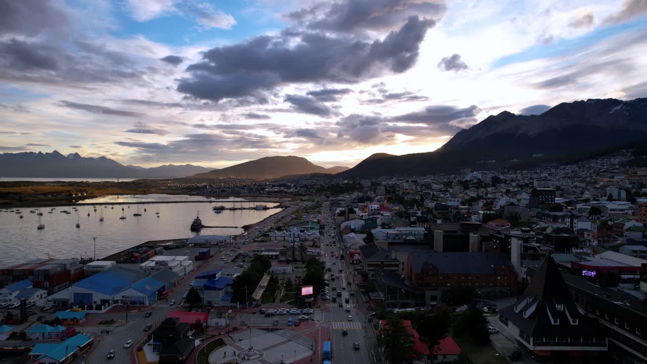Aerial Drone Footage Captures Ushuaia Village In Argentina, Showcasing The Beagle Channel Road. The Village Lies In Shadow As The Sun Sets Behind Mountains, Creating A Serene Summer Atmosphere.