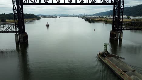 us, oregon, portland, st johns, 2025-07-26 - drone view of a barge being pushed by a tug on the willamette river under the raised railroad bridge