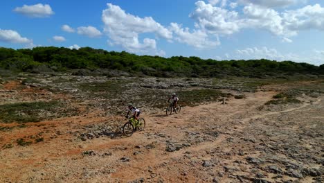 los corredores de btt en la carrera a lo largo de la costa de menorca, españa, encuentran los duros elementos del terreno rocoso un desafío.