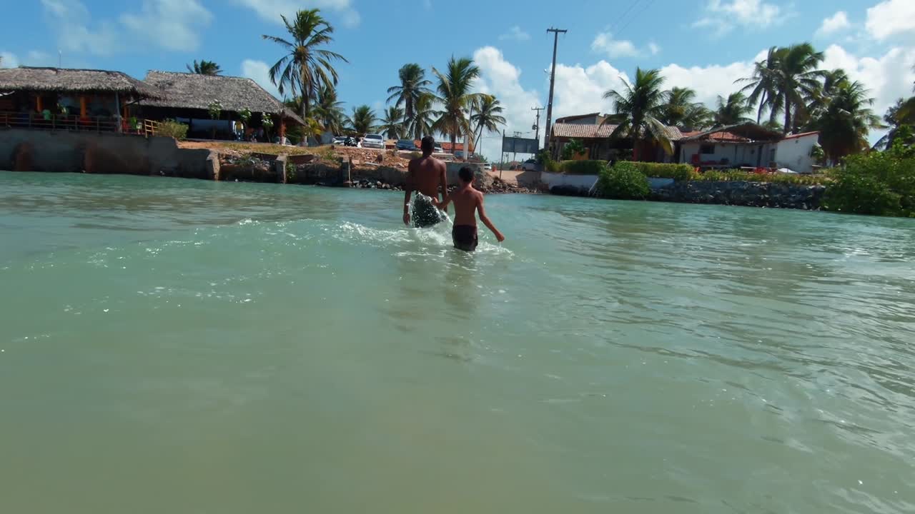 Due ragazzi brasiliani camminano in un fiume di un verde vibrante, giocando e schizzando a Sibauma, Rio Grande do Norte, Brasile, vicino a Pipa