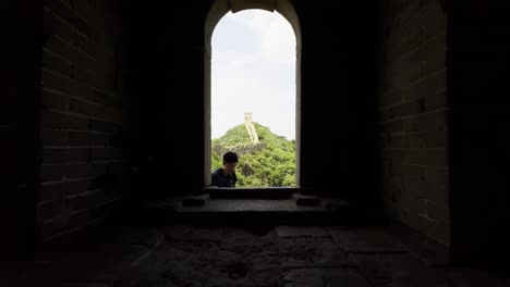 view from inside a watchtower on the great wall of china as a man enters through a small window, showcasing the great wall behind