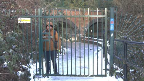 male guard closing heavy green iron park gate to deny entrance to snowy winter pathway