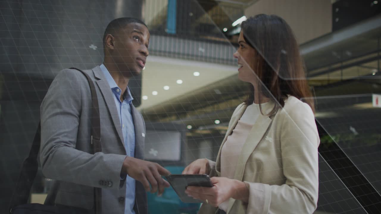 Man arriving with tablet, woman tapping screen in business atrium, blue HUD showing data, aligning