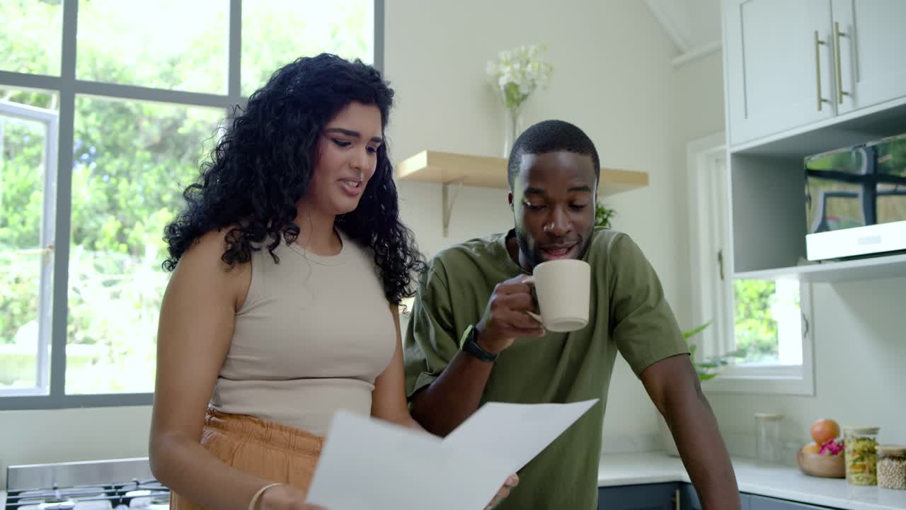 Diverse couple turning paper to man, pointing and reading at kitchen, finalizing review with tablet