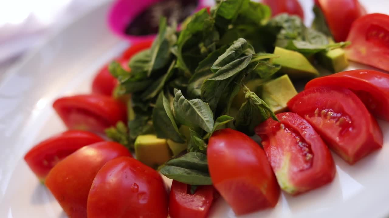 colpo al rallentatore di un'insalata di pomodoro basilico con avocado servito su un piatto bianco