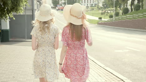 two women walking down the street in summer dresses and hats