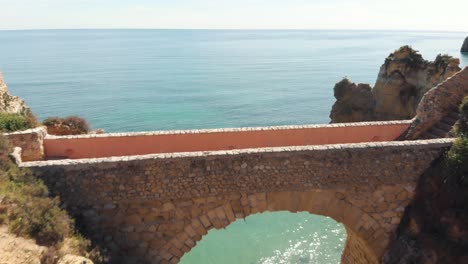 roman style bridge connecting two rock formations in lagos, algarve, portugal - aerial fly-by reveal shot