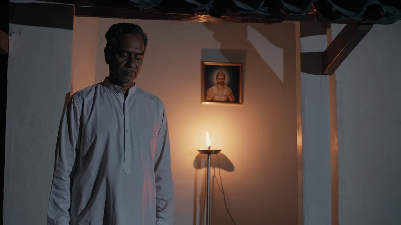 Indian priest standing with his head bowed in prayer, illuminated by the warm glow of a candle, in a serene Hindu temple setting, conveying a sense of devotion and spirituality