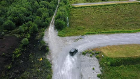 cinematic fast pace aerial drone camera footage, you can see a black jeep driving off-road at speed with dust in the air in countryside landscape surrounded by green fields