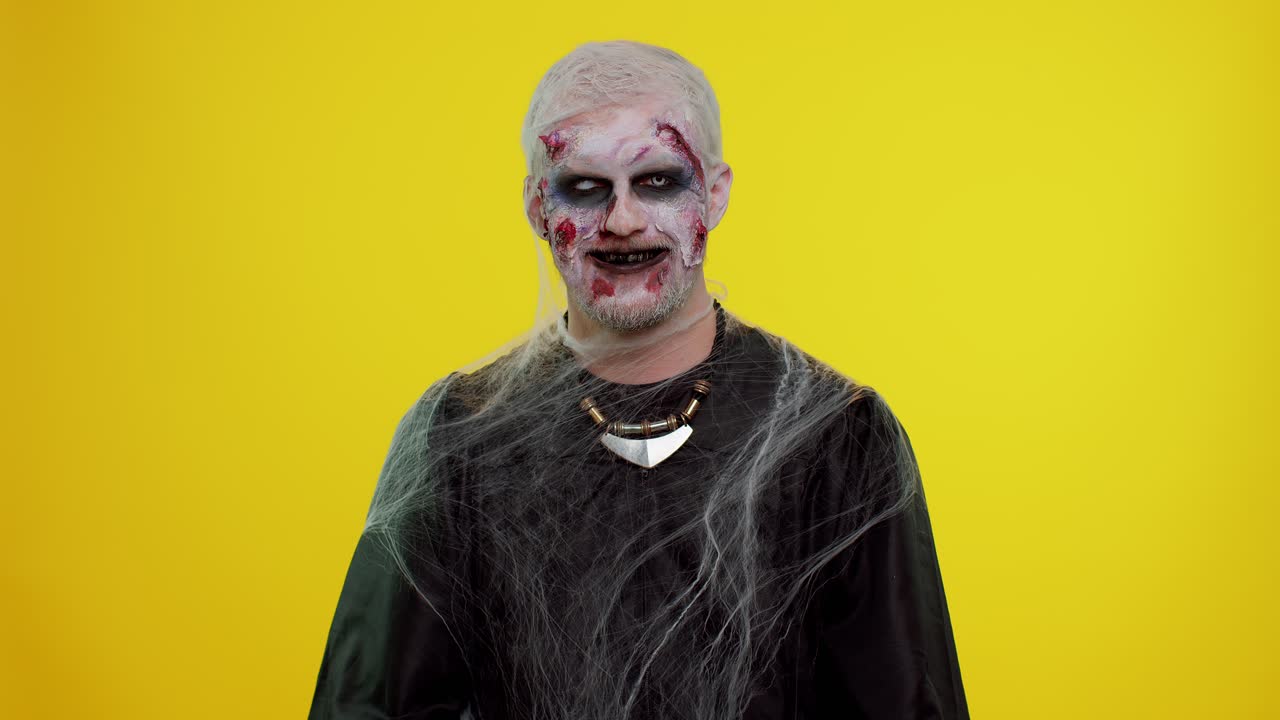 Cheerful creepy man Halloween zombie making faces, looks at camera, smiles terribly with dirty teeth