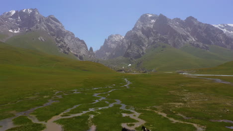 Vista-Aérea-De-Caballos-Galopando-A-Través-De-Un-Valle-Alpino-En-Las-Impresionantes-Montañas-De-Kirguistán