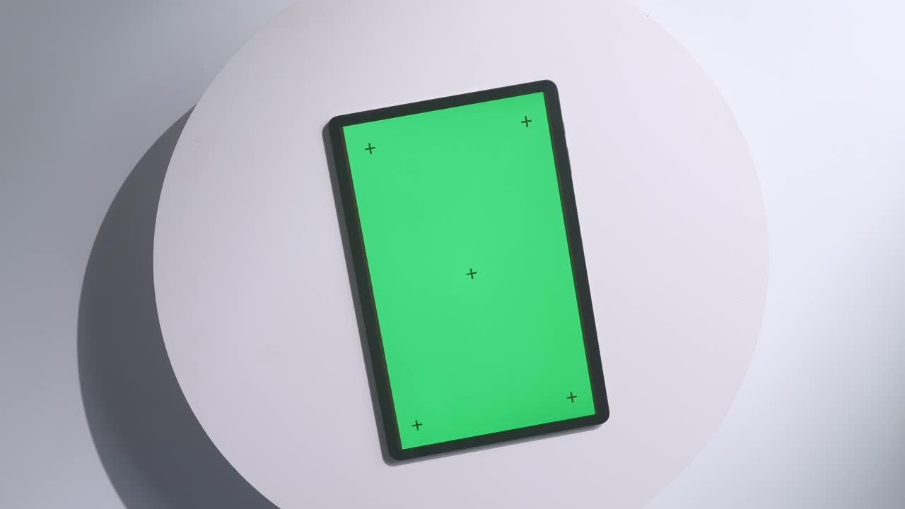 Top down view of a laptop computer with mock up green screen chromakey display on a wooden office desk next to notebook with pens, glasses, and a glass of water. Slow zoom out, close up