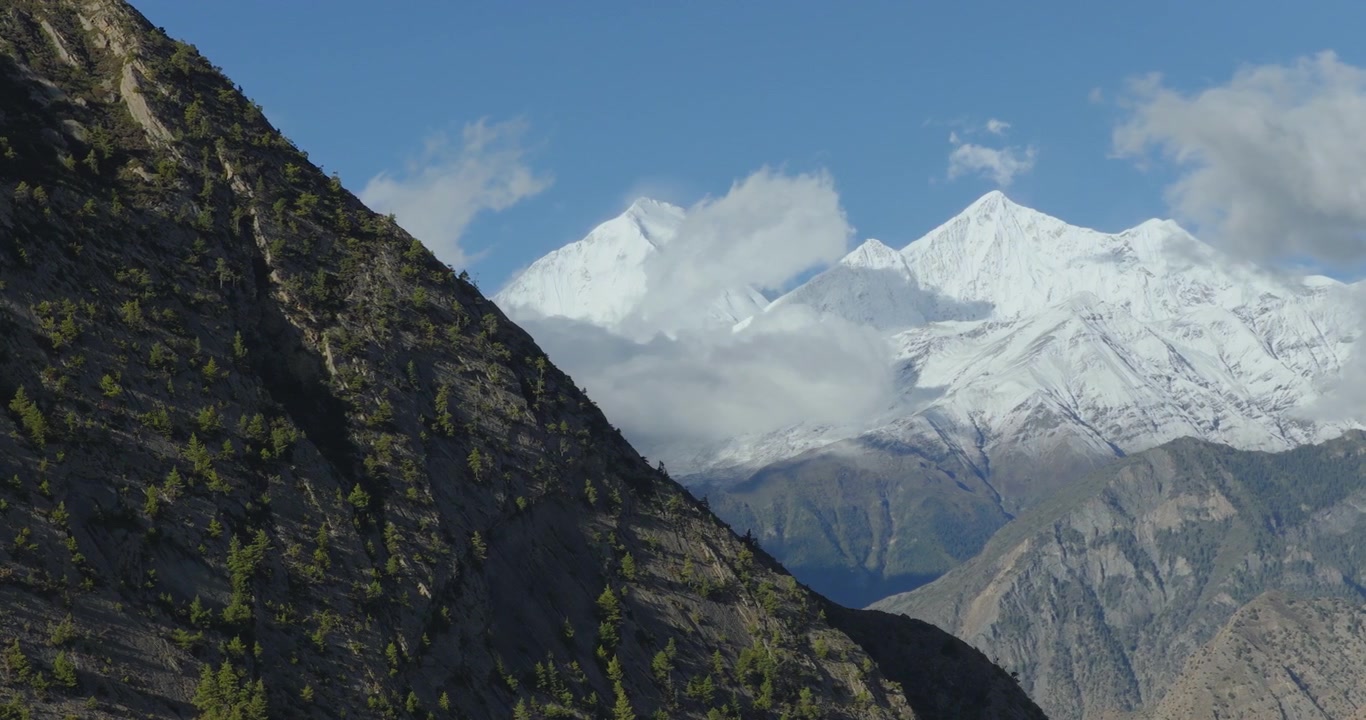 Boczne ujęcie z drona bujnych zielonych zboczy, zanim ukażą się pokryte śniegiem góry Nilgiri pod głębokim błękitnym niebem w Mustangu, Nepal.