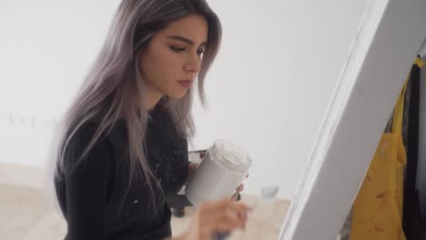 young beautiful painter standing and applying white acrylic paint on canvas in easel