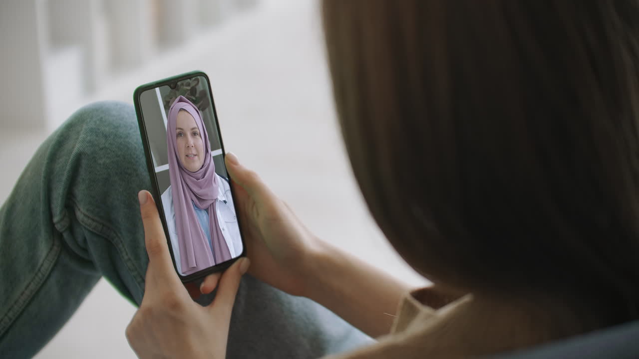 mujer usando una aplicación médica en un teléfono inteligente consultando con un médico árabe musulmán con hijab a través de videoconferencia. mujer usando un chat en línea para hablar con un terapeuta familiar y la pandemia de coronavirus.