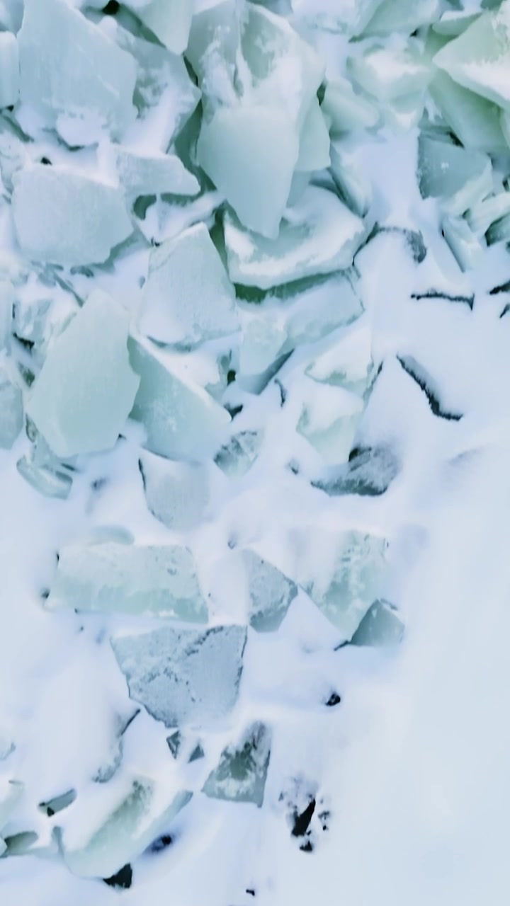 Vista verticale dall'alto con drone di impronte sparse sulla riva innevata e ghiacciata accanto a un canale scuro e ghiacciato, creando un sorprendente motivo di texture invernale