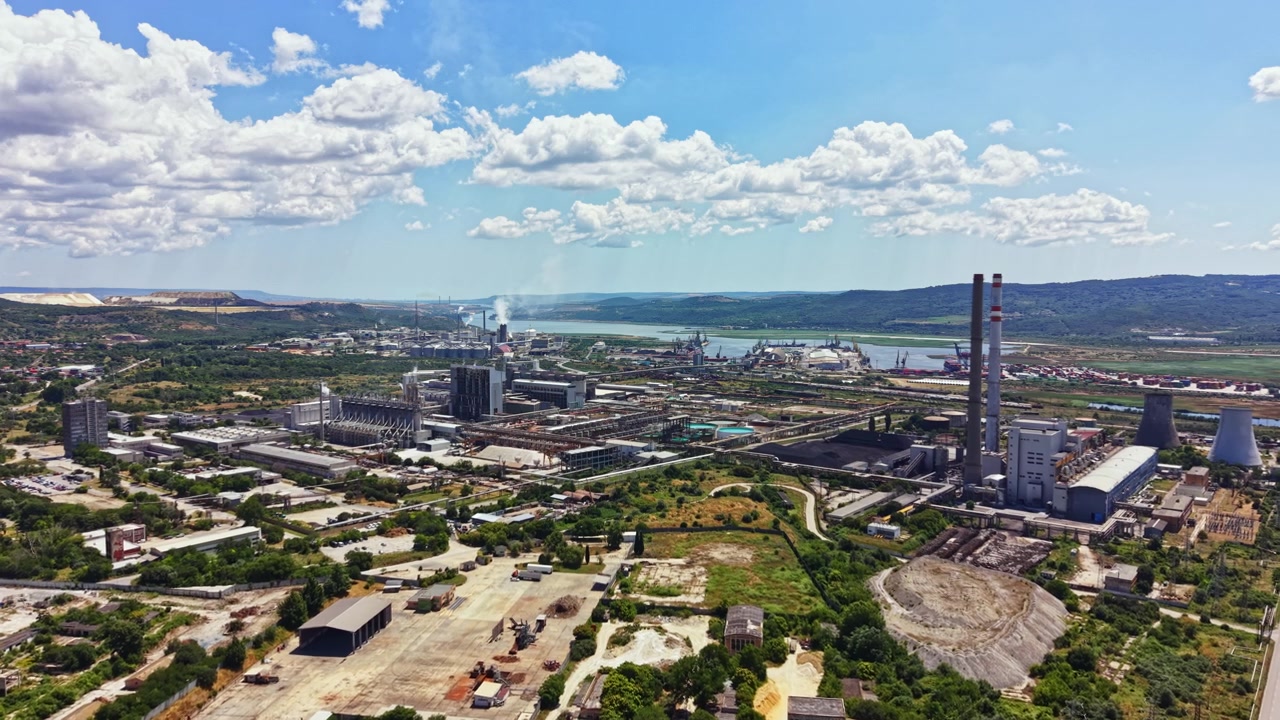 Paesaggio industriale che mostra fabbriche e impianti vicino al fiume sotto un cielo blu con nuvole in un pomeriggio estivo