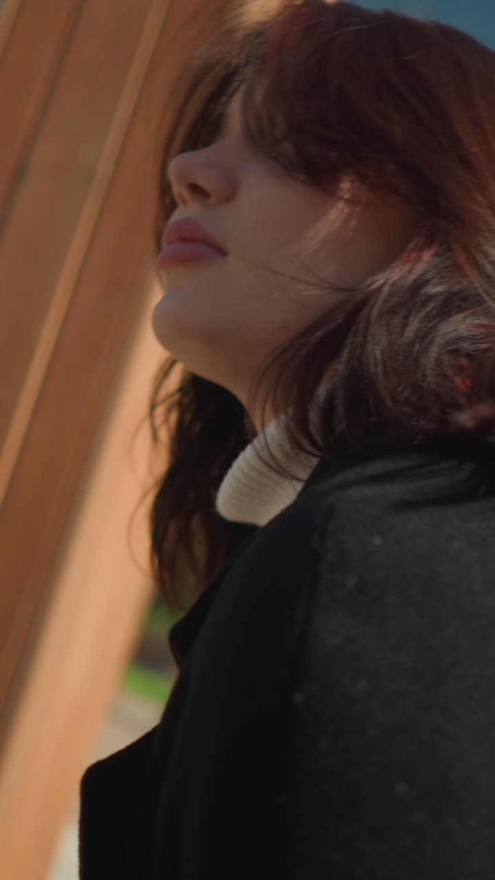 primer plano de una joven sonriendo y balanceándose al aire libre, su cabello balanceándose con la brisa mientras lo ajusta, rodeado de vegetación vibrante en un parque soleado y brillante