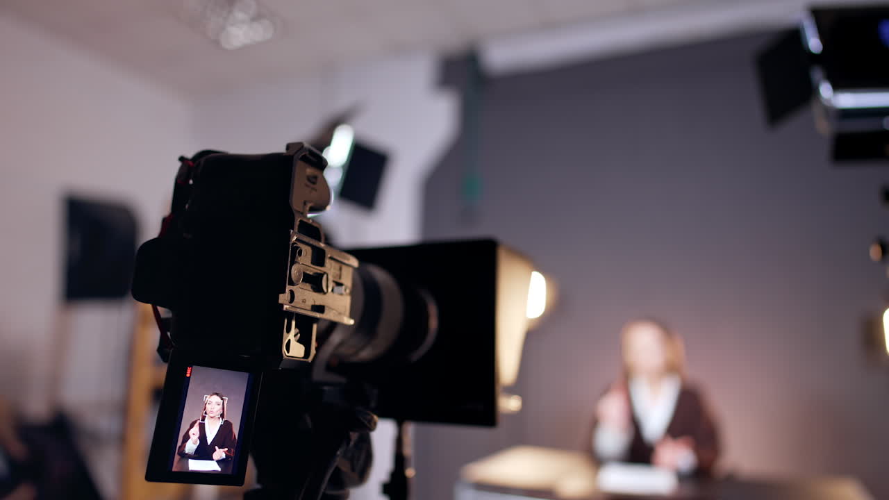 Camera recording a female blogger in the studio. Little display depicts a woman with long brown hair. Close up. Blurred backdrop.